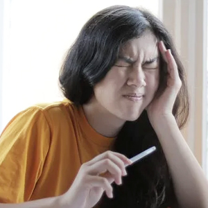 A woman sits on a couch while experiencing TMJ pain