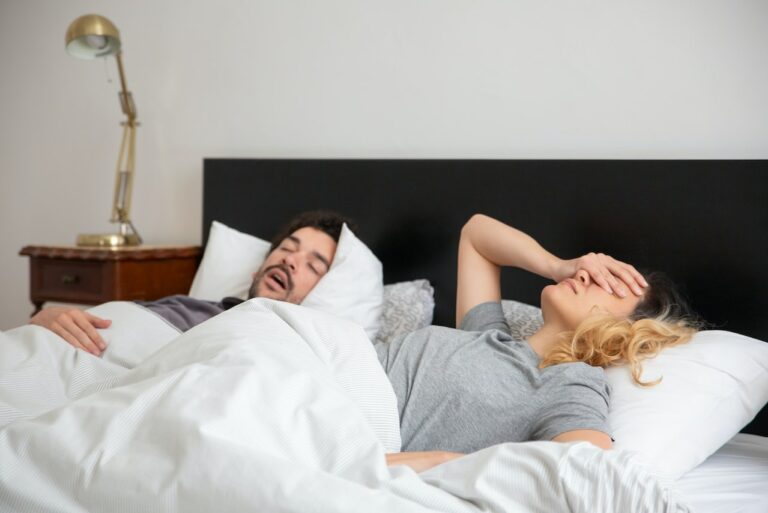 Man lying on his back snoring in bed while the woman beside him sleeps facing away