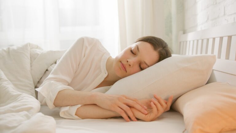 Woman sleeping peacefully on a white pillow in a sunlit bedroom