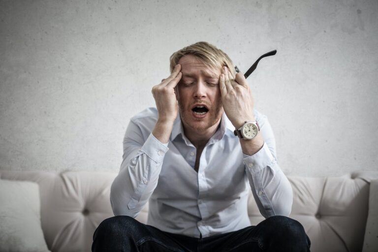 Man sitting with his eyes closed, both hands pressed to his forehead