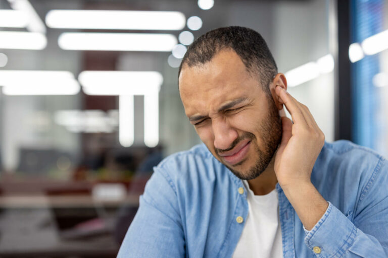 Young man in an office grimacing and cupping his hand over his ear