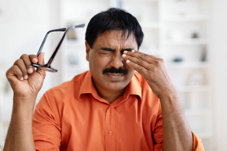 Man setting down his glasses to rub his closed eye and brow