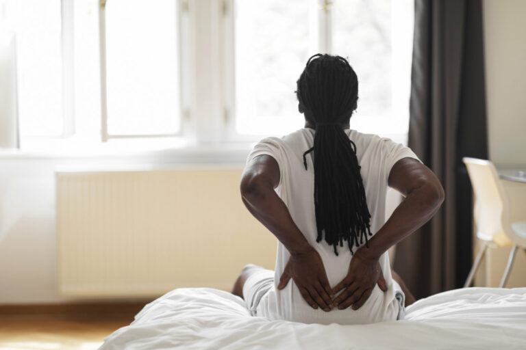 Man sitting on the edge of his bed after waking, holding his head