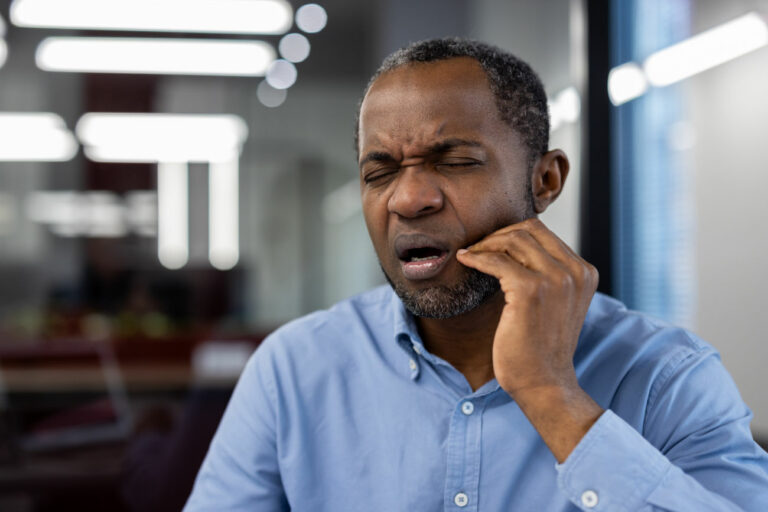 Man with a pained expression pressing his hand against his lower jaw