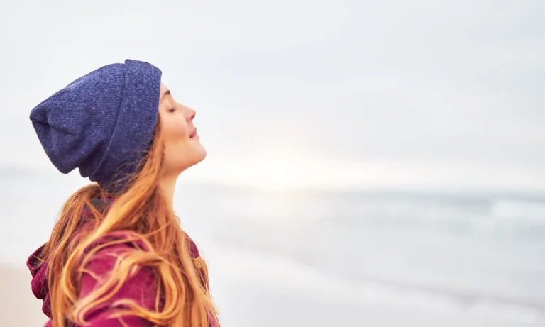 Woman in a knitted beanie tilting her head back to breathe in fresh air outdoors