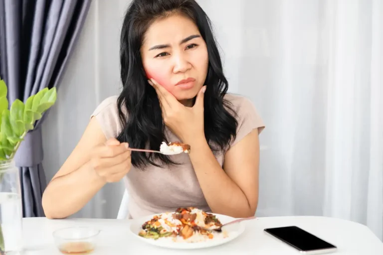 Woman pausing mid-bite at a dinner table, holding her cheek in pain