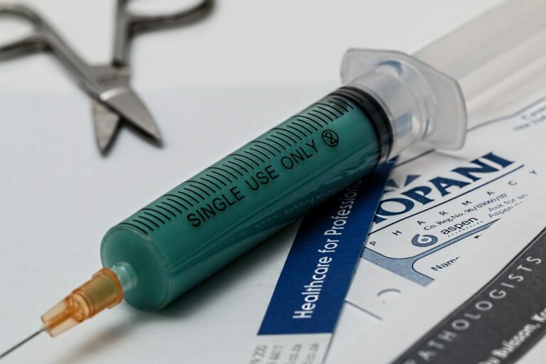 Close-up of a filled single-use syringe resting on medical paperwork next to steel forceps