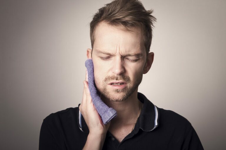 Man wincing with his eyes shut while pressing a folded purple cloth against the side of his jaw