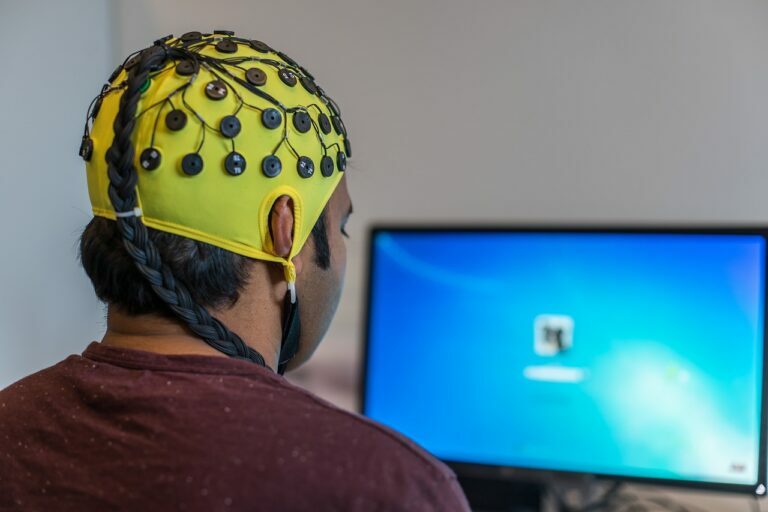 Man wearing a yellow EEG electrode cap facing a computer screen during a brainwave session