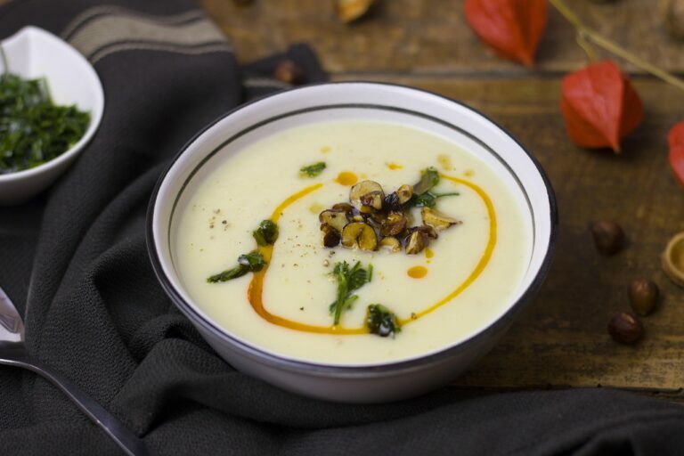 Bowl of smooth cream soup garnished with herbs, set on a dark napkin beside a spoon