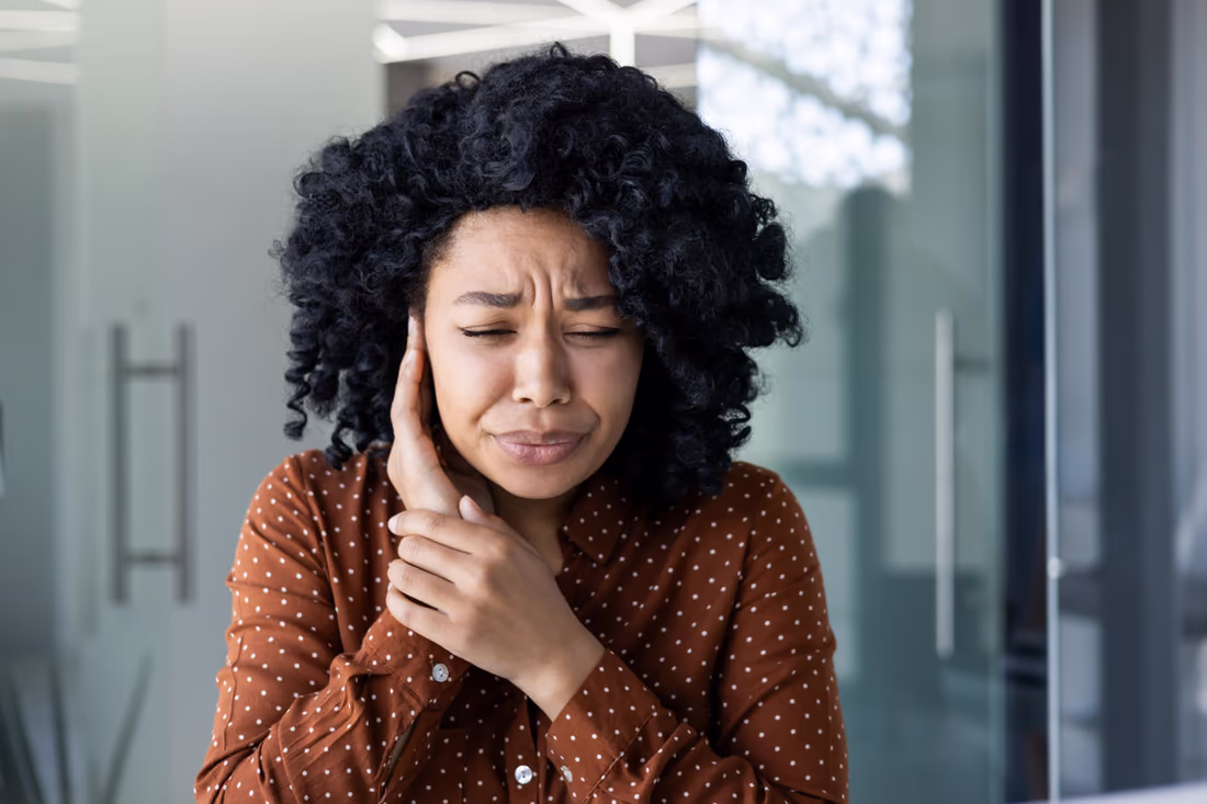 Chronic jaw and facial pain Woman wincing with her hand held against her jaw and ear from persistent facial pain