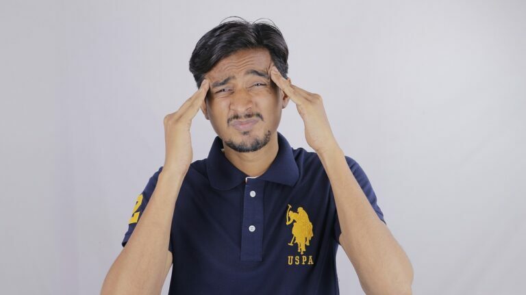 Man in a navy polo shirt pressing his fingertips into both temples with his eyes closed
