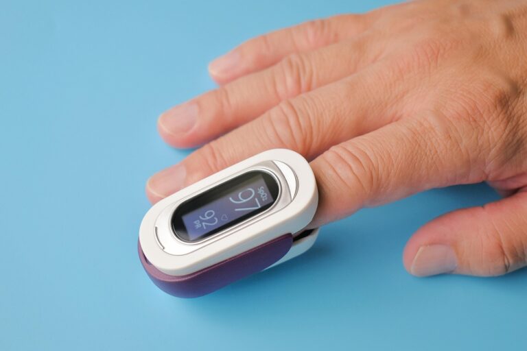 Fingertip pulse oximeter clipped to a hand on a blue background, showing an oxygen reading of 97