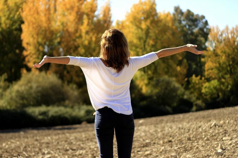 Woman standing with her arms outstretched in a ploughed field on an autumn day