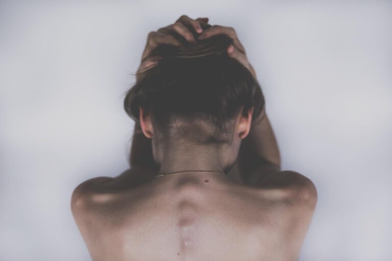 Woman photographed from behind gripping her hair with both hands, shoulders tense